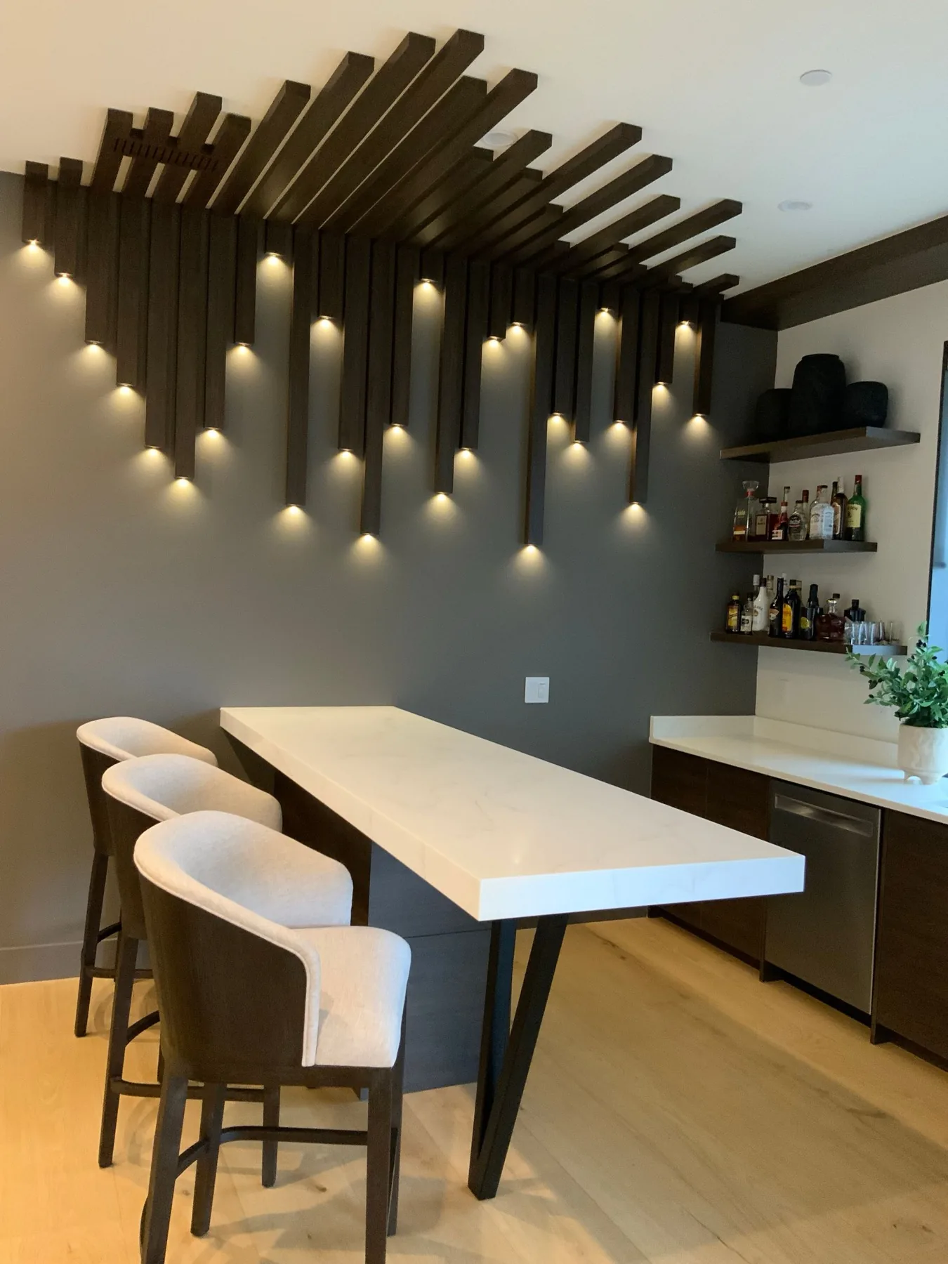 Dining bar with upholstered stools under a sculpted slat ceiling.
