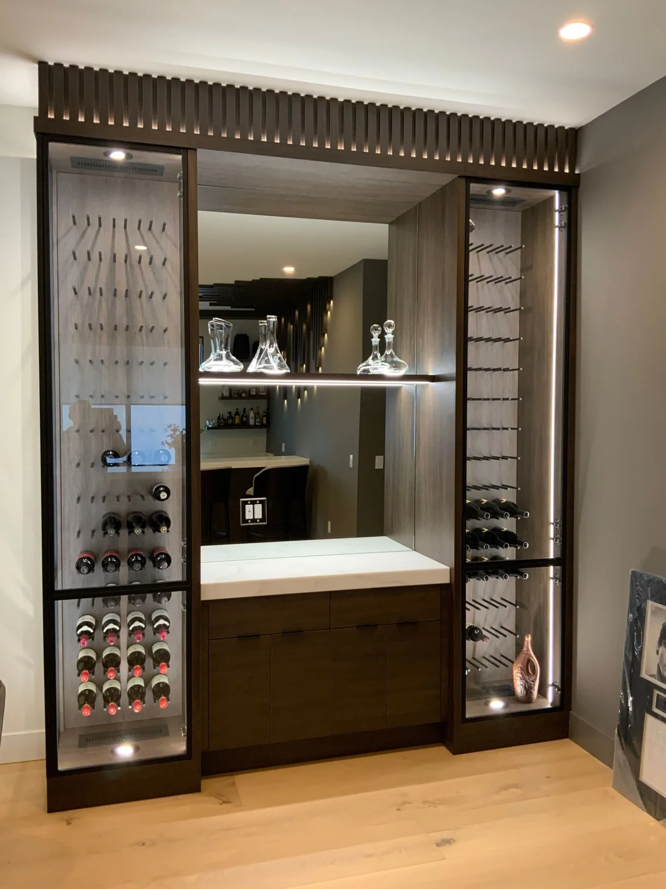 Built-in wine storage with lit glass cabinets either side of a stone bar counter.